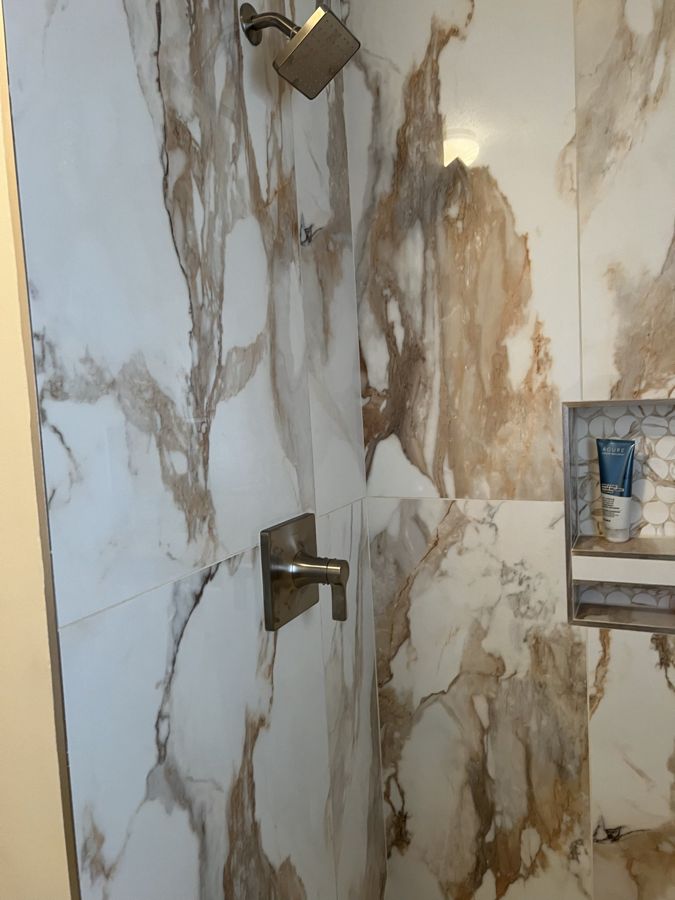 New shower valve and showerhead in a marble-look tile shower