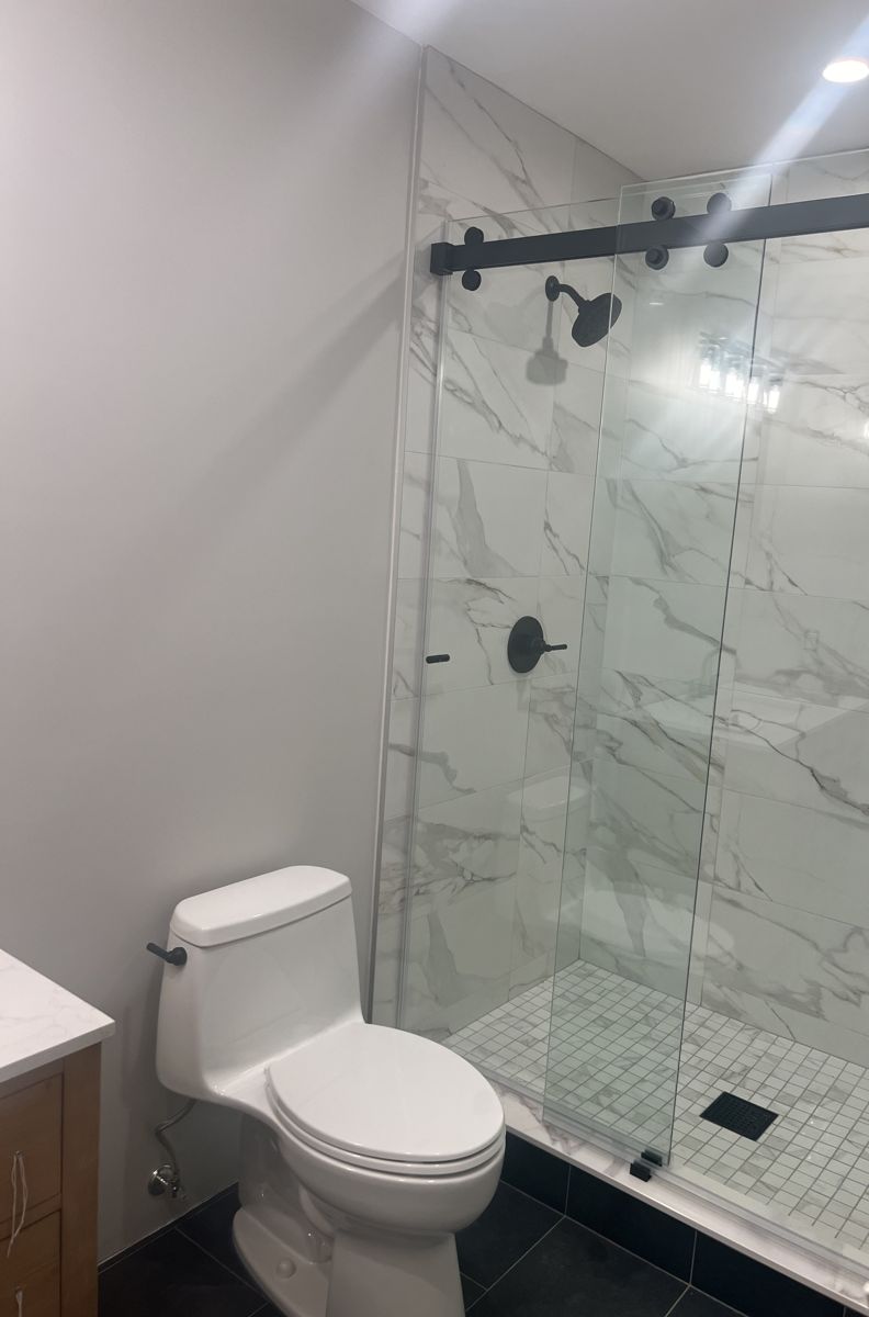 Remodeled bathroom with one-piece toilet, glass shower and dark floor tile
